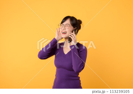 Portrait young Asian woman 30s wearing purple shirt and glasses receive an exited news from mobile phone isolated on yellow background. Great news concept. 113239105