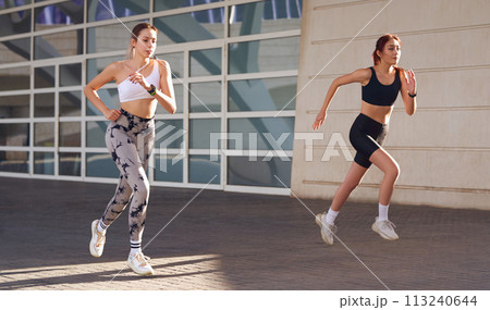 Two active women athlete running on sunny morning side by side on modern buildings background 113240644