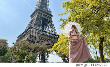 a girl with a white parasol stands against the backdrop of the Eiffel Tower with her back to us can be used for advertising for the Internet for travel agencies 113242079