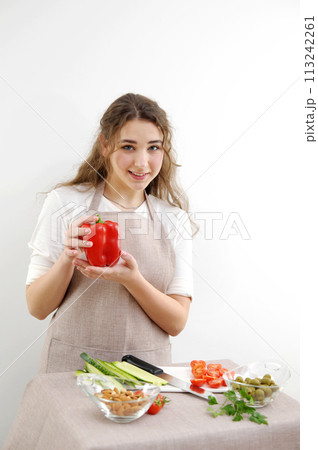 Smiling brunette woman holding red bell pepper while standing with hand on hip Green vegan salad with mixed green leaves and vegetables Green salad with tomatoes and fresh vegetables Smiling brunette woman holding red bell pepper while standing with hand on hip Green vegan salad with mixed green leaves and vegetables Green salad with tomatoes and fresh vegetables 113242261