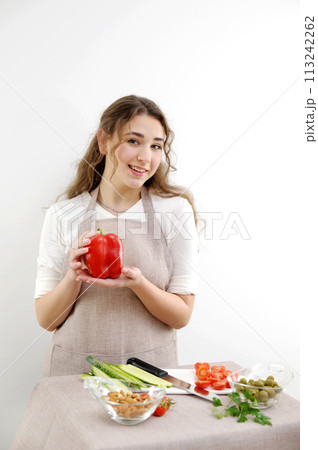 a young woman stands in her hands with red pepper looks at us prepares a delicious salad the choice of proper nutrition the desire to be healthy and beautiful a young woman stands in her hands with red pepper looks at us prepares a delicious salad the choice of proper nutrition the desire to be healthy and beautiful 113242262