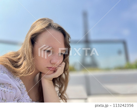 the face of a beautiful girl she is sad leaning on her arm in the distance you can see the Eiffel Tower the girl is young she is a teenager 113242356