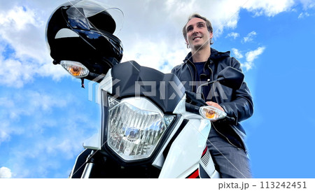 male biker sits on a motorcycle against the background of nature and mountain he in a leather jacket on the handlebars of a motorcycle is wearing a helmet male biker sits on a motorcycle against the background of nature and mountain he in a leather jacket on the handlebars of a motorcycle is wearing a helmet 113242451
