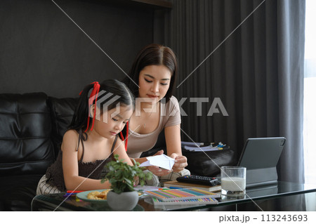 Beautiful young mother working at home and playing with daughter in living room Beautiful young mother working at home and playing with daughter in living room 113243693