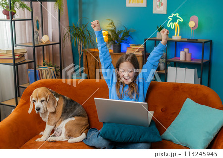 Happy child girl using laptop typing playing game good positive news celebrate online win at home 113245945