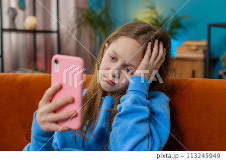 Upset child kid girl using smartphone playing game loses bad news fail education study test at home 113245949