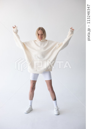 Beautiful blonde woman posing in white hoodie and leggings posing against white background 113246347