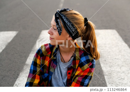 Portrait of a teenage girl wearing a stylish bandana and a cheerful smile, standing confidently on a country road, exuding youthfulness and a sense of adventure 113246864