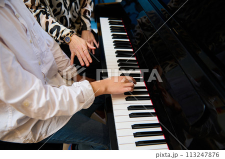 Selective focus to teenage boy musician pianist fingers and piano key to play the piano. Close-up child playing the piano during individual music lesson under his teacher's guidance 113247876