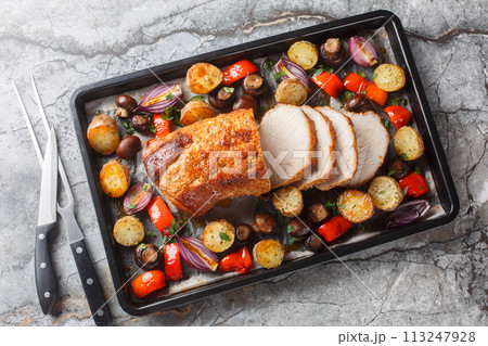 Delicious festive baked pork loin with vegetables and mushrooms close-up on a baking sheet. Horizontal top view 113247928