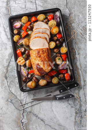 Baked pork loin with vegetables and mushrooms close-up on a baking sheet. Vertical top view Baked pork loin with vegetables and mushrooms close-up on a baking sheet. Vertical top view 113247930