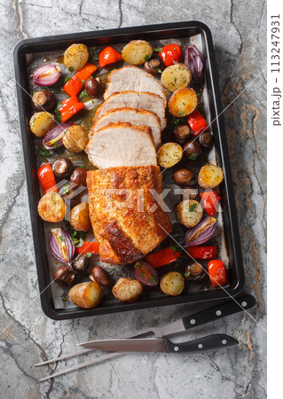 Festive baked pork loin with potatoes, onions, peppers and mushrooms close-up on a baking sheet. Vertical top view Festive baked pork loin with potatoes, onions, peppers and mushrooms close-up on a baking sheet. Vertical top view 113247931