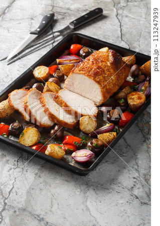 Festive baked pork loin with potatoes, onions, peppers and mushrooms close-up on a baking sheet. Vertical 113247939