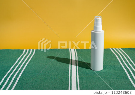 Blank white sunscreen bottle on green Turkish beach towel in direct sunlight. Summer skin protection mockup template with reading beach aesthetic 113248608