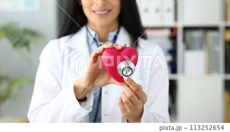 Hands of female GP holding stethoscope head near red toy heart 113252654