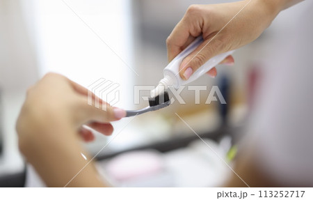 Female hand squeezing toothpaste from tube onto toothbrush close-up 113252717