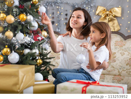 Mom and daughter holding Christmas decorations on Christmas tree 113253952