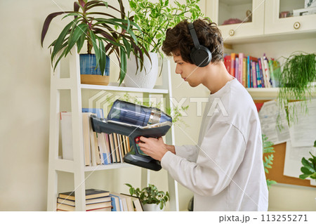 Young man wearing headphones vacuums bookshelves at home Young man wearing headphones vacuums bookshelves at home 113255271