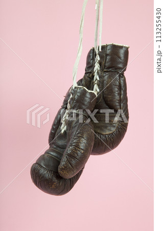 a pair of old boxing gloves hung in front of a candy-pink background 113255430