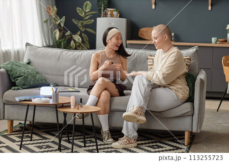 Wide shot of joyful Asian and Caucasian girls spending time together at home sitting on couch in living doing manicure and laughing at funny story Wide shot of joyful Asian and Caucasian girls spending time together at home sitting on couch in living doing manicure and laughing at funny story 113255723