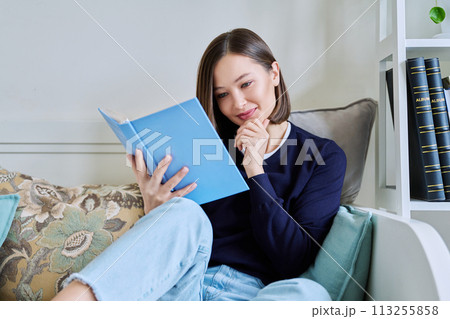 Young woman reading book, relaxed sitting on couch at home Young woman reading book, relaxed sitting on couch at home 113255858