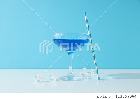 Blue cocktail in glass, straw and ice cubes on blue background 113255964