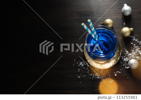 Blue cocktail with straws in glass, snow and balls on wooden background, space for text 113255981