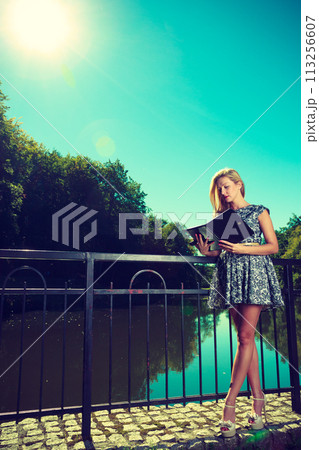 Woman sitting in park, relaxing and using tablet 113256607