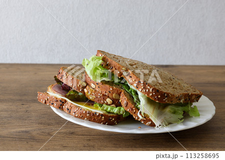 木材背景の皿にのせたオーガニックパンのサンドイッチ 113258695