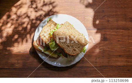 木材背景の皿にのせたオーガニックパンのサンドイッチ 113258696