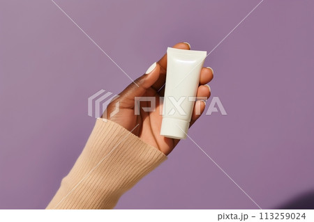 African American womans hand holds white tube on purple background. Skin health care concept African American womans hand holds white tube on purple background. Skin health care concept 113259024