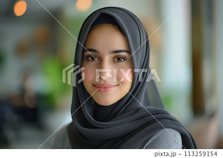 Portrait of young smiling Arabian muslim woman in grey hijab on blurred background 113259154