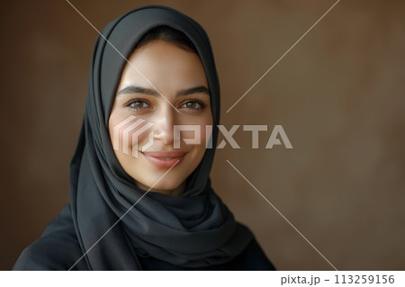 Portrait of young smiling Arabian muslim woman in black hijab on brown background with copy space 113259156
