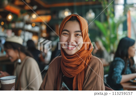 Portrait of young smiling muslim Asian woman wearing hijab and casual clothes sitting in the cafe 113259157