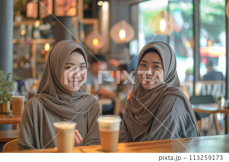 Portrait of two young muslim Asian women wearing beige abaya drinking coffee in the cafe Portrait of two young muslim Asian women wearing beige abaya drinking coffee in the cafe 113259173