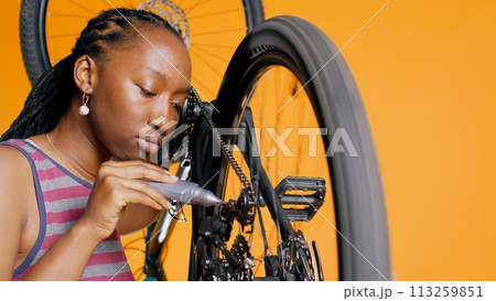 BIPOC technician using specialized glue to repair broken bicycle chain, orange studio background. Professional applying adhesive on bike components during maintenance process, close up shot, camera B BIPOC technician using specialized glue to repair broken bicycle chain, orange studio background. Professional applying adhesive on bike components during maintenance process, close up shot, camera B 113259851