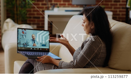 Patient sitting on couch, receiving treatment plan from medic during online videocall meeting after medical checkup. Indian person receiving prescription from GP in telemedicine call, camera B 113259877