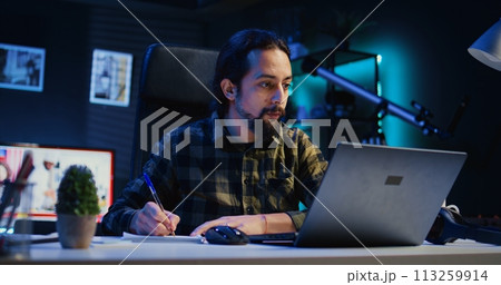 Man at home paying attention in elearning seminar on laptop to online class teacher, writing down information. Homeschooling student listening to internet course lesson and doing homework 113259914