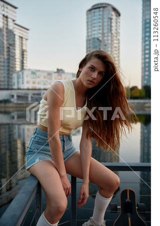 Young woman skateboarder dressed in casual attire taking break 113260548