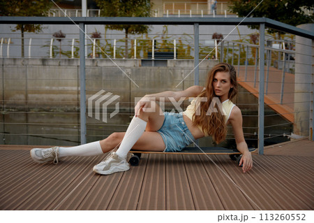 Young woman dressed casual teenage wear lying on skateboard 113260552