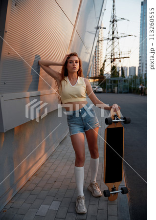 Young woman with longboard standing over cityscape background 113260555
