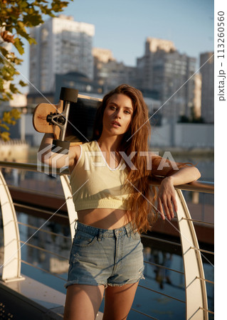 Sensual slim woman with longborad on shoulder posing for camera in city park 113260560