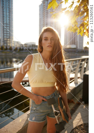 Cool young woman skateboarder standing over sunset in urban park 113260561