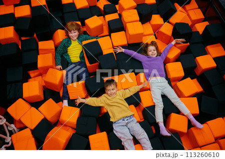 Happy children lying in dry pool with soft cube in entertainment center Happy children lying in dry pool with soft cube in entertainment center 113260610