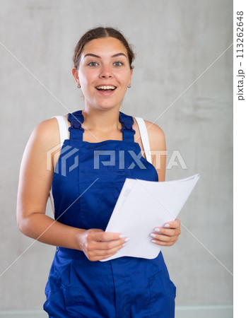 Young woman in work overalls posing with documents Young woman in work overalls posing with documents 113262648
