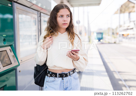 Confident girl walking along a tram stop holds a mobile phone 113262702