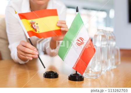 Little flag of Iran on table and flag of Spain put next to it by young woman 113262703