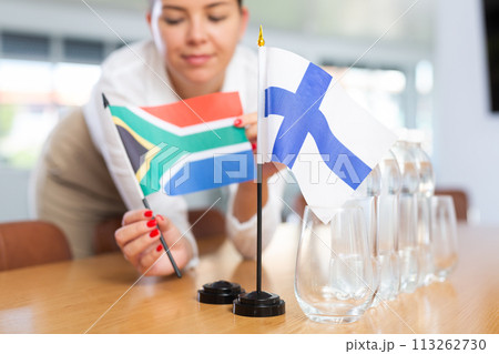 Woman secretary prepares an office for negotiations - she places flags of Finland and South Africa table 113262730