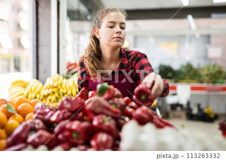 Young positive woman seller lay out ripe pepper on the counter 113263332