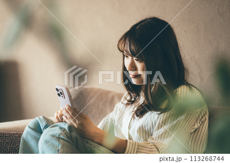 ソファでスマホを使う笑顔の女性 ソファでスマホを使う笑顔の女性 113268744